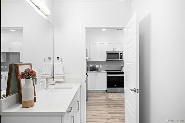 kitchen with light wood finished floors, white cabinetry, appliances with stainless steel finishes, and backsplash