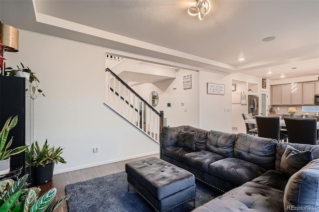 living area with baseboards, a textured ceiling, wood finished floors, and stairs