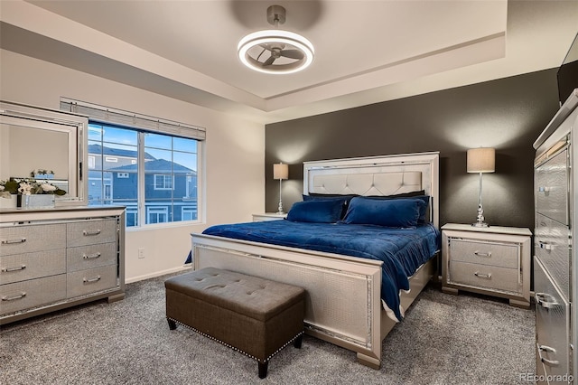 bedroom featuring dark colored carpet, baseboards, and a raised ceiling