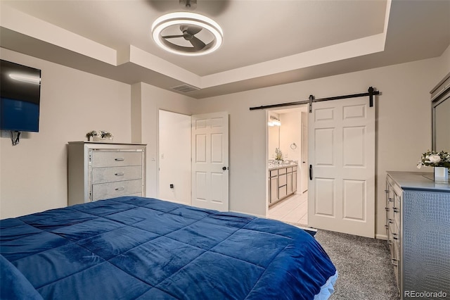 bedroom featuring a tray ceiling, a barn door, carpet floors, and visible vents