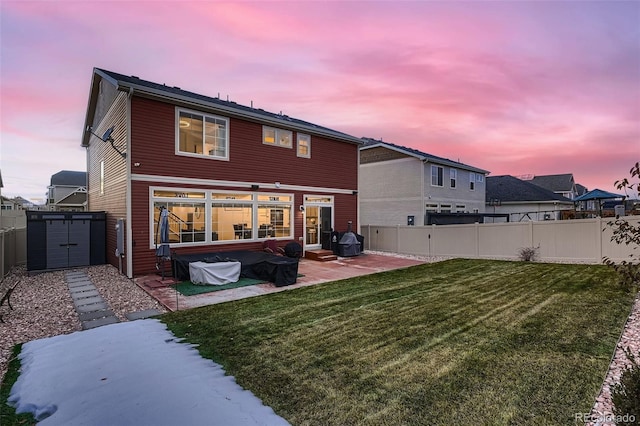 back of house at dusk featuring an outbuilding, a yard, a fenced backyard, a storage shed, and a patio area