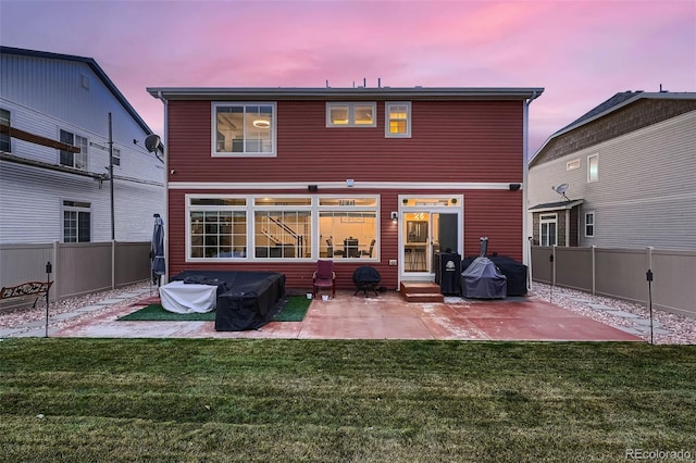 back of house at dusk featuring entry steps, a yard, a patio area, and a fenced backyard