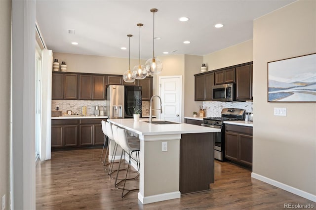 kitchen featuring sink, hanging light fixtures, an island with sink, dark brown cabinets, and appliances with stainless steel finishes