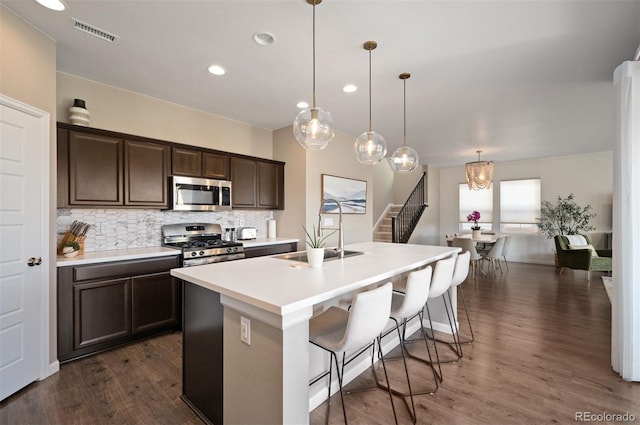 kitchen featuring tasteful backsplash, stainless steel appliances, sink, pendant lighting, and an island with sink