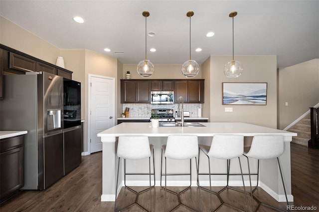 kitchen with decorative light fixtures, tasteful backsplash, stainless steel appliances, and an island with sink