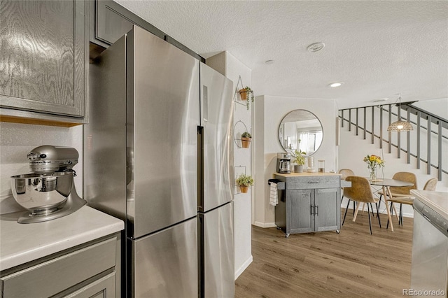 kitchen featuring gray cabinetry, light hardwood / wood-style flooring, stainless steel fridge, a textured ceiling, and decorative light fixtures