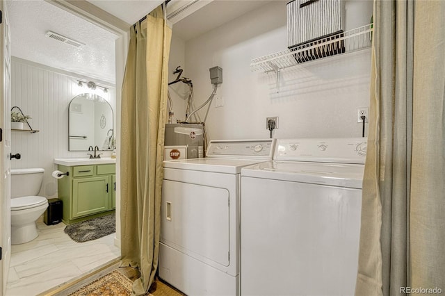 clothes washing area with electric water heater, washer and clothes dryer, a textured ceiling, and wooden walls