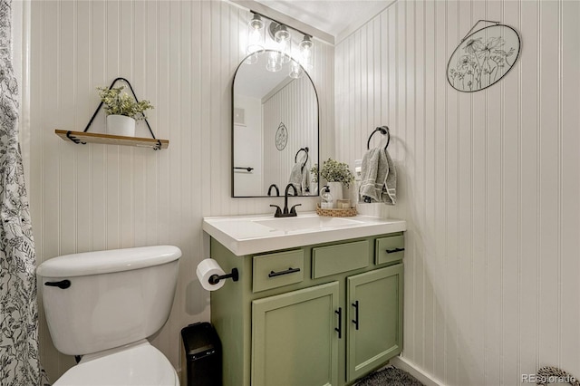 bathroom featuring vanity, wood walls, and toilet