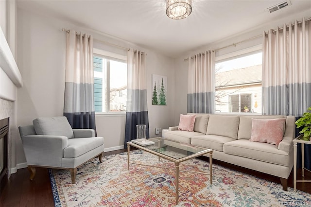 living room featuring a glass covered fireplace, visible vents, baseboards, and wood finished floors