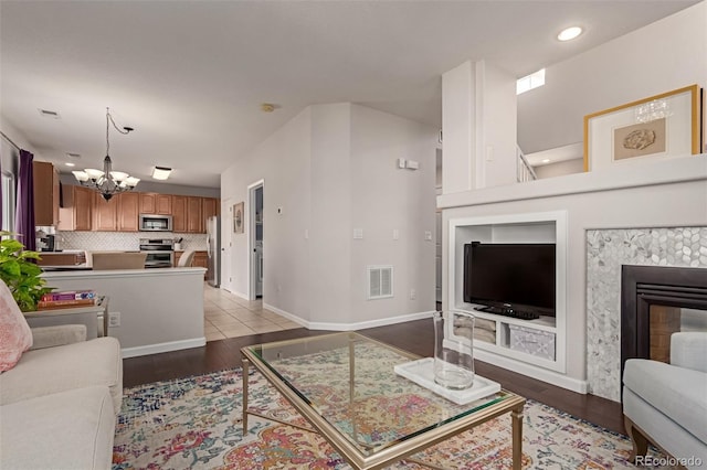 living area with baseboards, visible vents, wood finished floors, a notable chandelier, and a high end fireplace