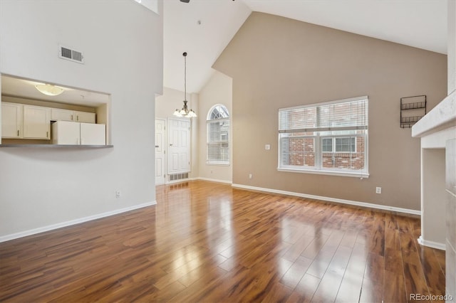 unfurnished living room with a notable chandelier, high vaulted ceiling, baseboards, wood finished floors, and visible vents