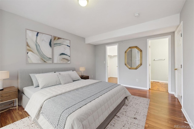 bedroom featuring baseboards, wood finished floors, and a spacious closet