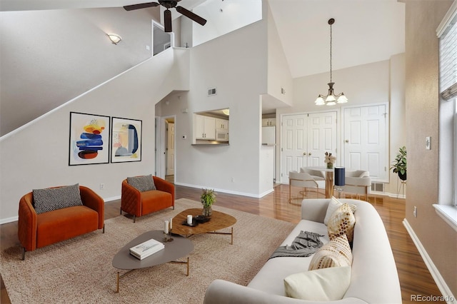 living room with high vaulted ceiling, ceiling fan with notable chandelier, wood finished floors, and visible vents