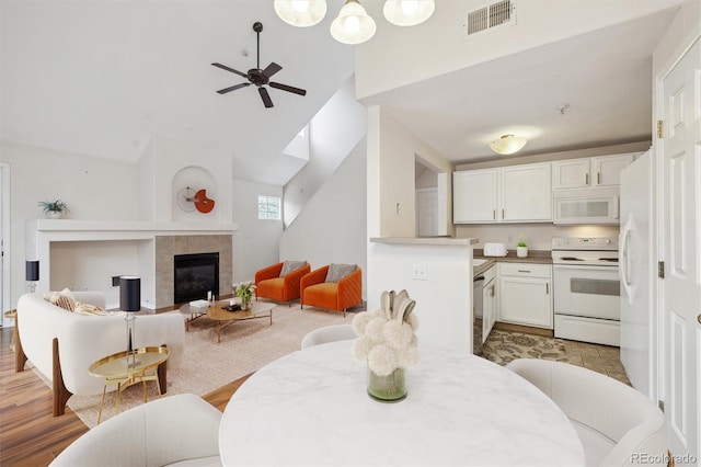 dining area with ceiling fan, high vaulted ceiling, light wood-style flooring, a tile fireplace, and visible vents