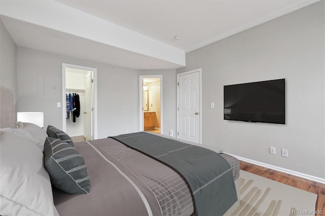 bedroom featuring a walk in closet, baseboards, wood finished floors, ensuite bathroom, and a closet