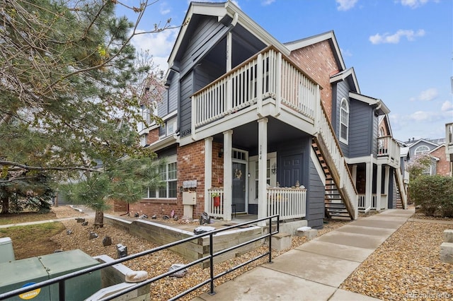 view of front facade featuring brick siding, stairs, a balcony, and a porch