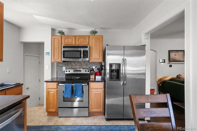 kitchen with appliances with stainless steel finishes, decorative backsplash, light tile patterned floors, and a textured ceiling