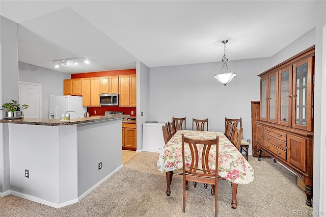 kitchen featuring stainless steel microwave, white refrigerator with ice dispenser, brown cabinetry, dark countertops, and glass insert cabinets