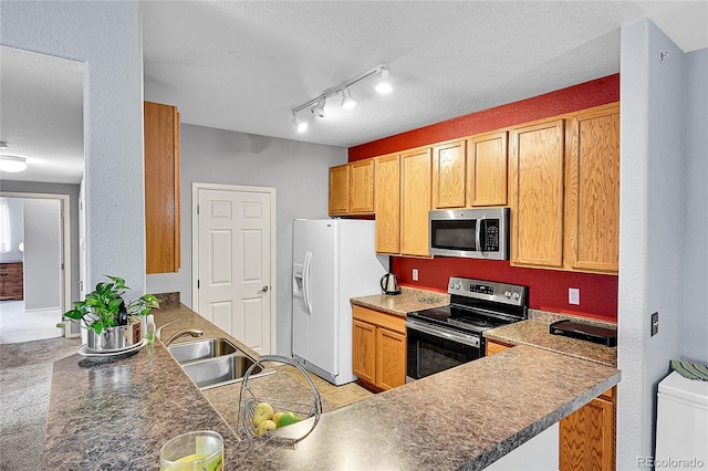 kitchen with a textured ceiling, a peninsula, a sink, appliances with stainless steel finishes, and dark countertops