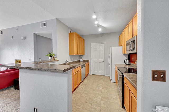 kitchen with dark countertops, visible vents, appliances with stainless steel finishes, a sink, and a peninsula