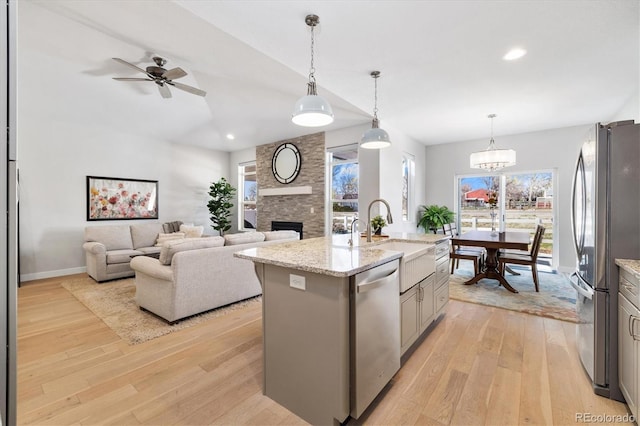 863 Shirttail Peak Dr, Windsor, CO 80550 - kitchen featuring appliances with stainless steel finishes, a sink, a fireplace, light wood finished floors, and an island with sink