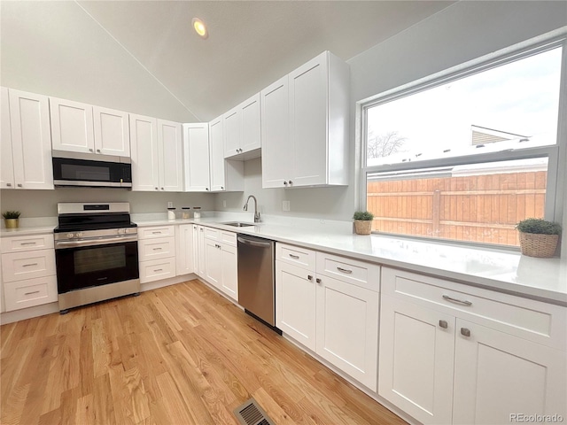 kitchen with light countertops, light wood-style flooring, appliances with stainless steel finishes, white cabinetry, and a sink