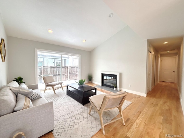 living area with lofted ceiling, recessed lighting, a fireplace with flush hearth, light wood-type flooring, and baseboards