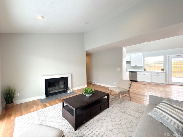 living room with lofted ceiling, a fireplace with flush hearth, visible vents, baseboards, and light wood finished floors