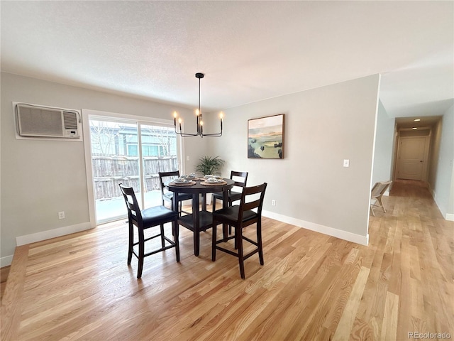 dining room with a wall unit AC, light wood finished floors, baseboards, and a chandelier