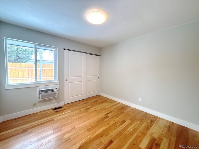 unfurnished bedroom featuring a wall unit AC, visible vents, baseboards, light wood-style floors, and a closet