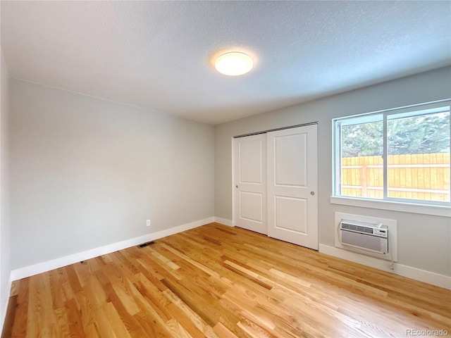 unfurnished bedroom featuring baseboards, a wall unit AC, visible vents, and light wood finished floors