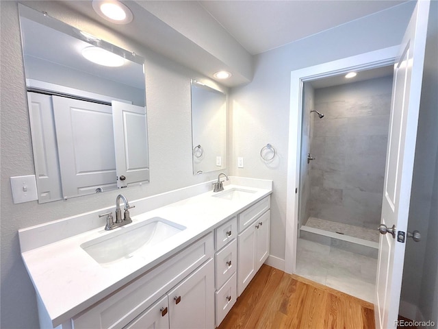 full bath with double vanity, wood finished floors, a sink, and a shower stall