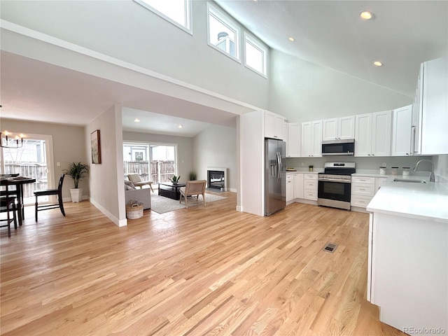 kitchen with a sink, white cabinets, open floor plan, light countertops, and appliances with stainless steel finishes