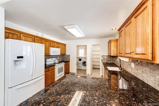 kitchen with sink, dark stone counters, a textured ceiling, white appliances, and washer and clothes dryer