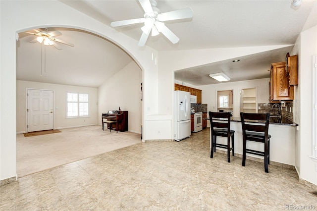 kitchen with ceiling fan, light colored carpet, white appliances, and vaulted ceiling