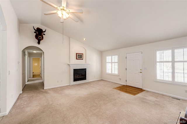 unfurnished living room featuring a tiled fireplace, ceiling fan, light carpet, and lofted ceiling