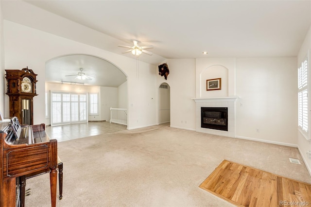 carpeted living room with a tiled fireplace, ceiling fan, and lofted ceiling