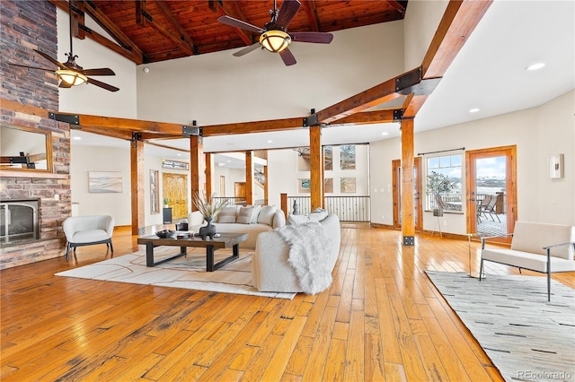 living room with beam ceiling, light hardwood / wood-style floors, a large fireplace, and ceiling fan