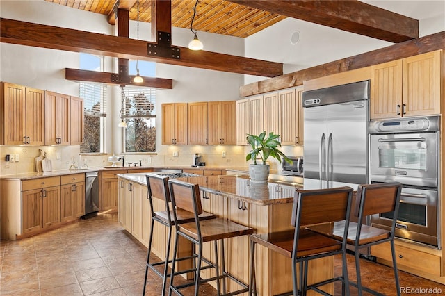 kitchen with a kitchen bar, tasteful backsplash, a center island, appliances with stainless steel finishes, and beamed ceiling