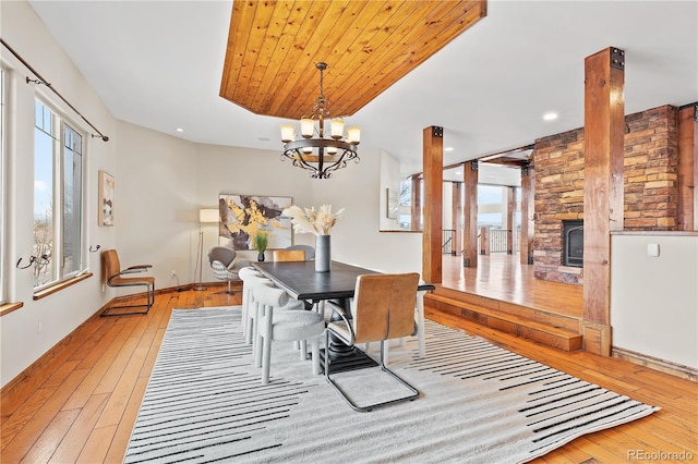 dining room featuring a stone fireplace, wood ceiling, a chandelier, light wood-type flooring, and a raised ceiling