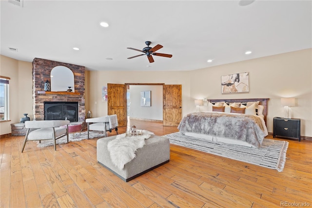 bedroom featuring ceiling fan, a large fireplace, and light wood-type flooring