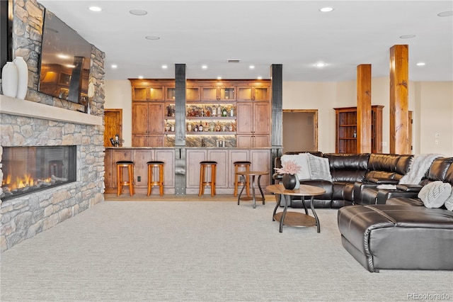 carpeted living room featuring bar and a stone fireplace