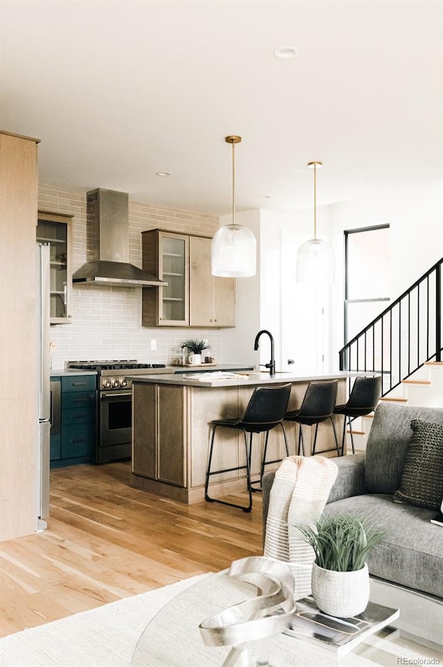 2753 Curtis St, Denver, CO 80205 - kitchen with light wood-type flooring, stainless steel appliances, a kitchen bar, wall chimney exhaust hood, and tasteful backsplash