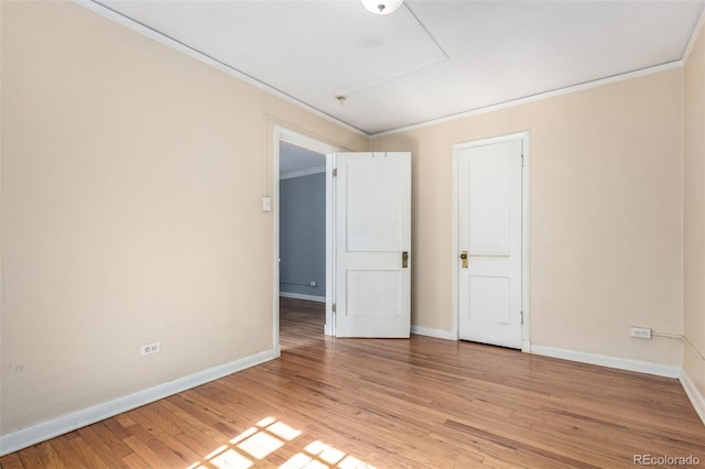 empty room featuring ornamental molding, light wood-type flooring, and baseboards