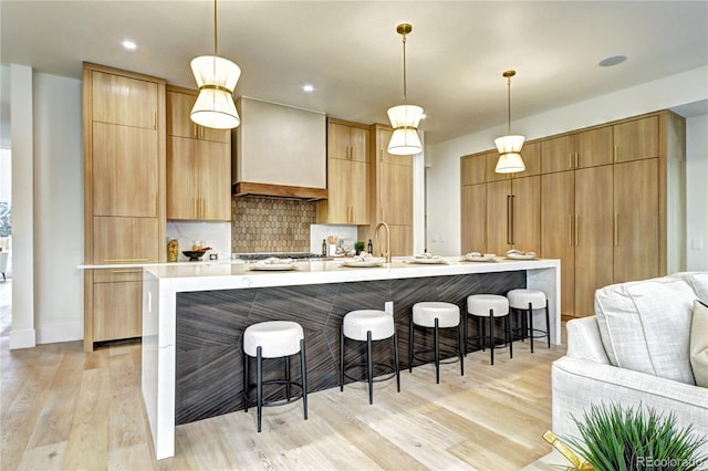 kitchen featuring a breakfast bar, a spacious island, decorative light fixtures, premium range hood, and decorative backsplash