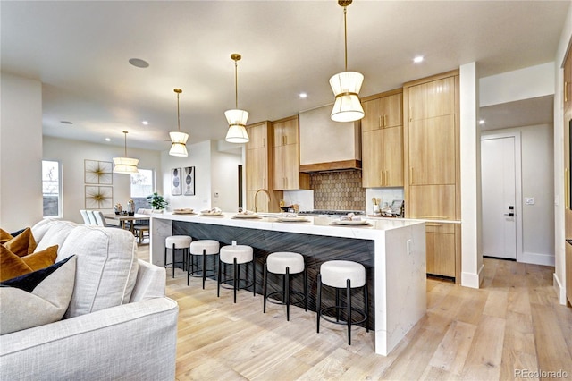 kitchen with pendant lighting, a kitchen island with sink, a breakfast bar area, and light brown cabinets