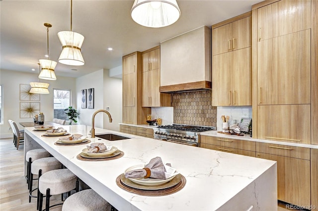 kitchen featuring a kitchen island with sink, sink, range with two ovens, custom range hood, and light brown cabinetry