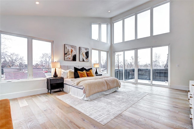 bedroom with light hardwood / wood-style flooring, a high ceiling, and access to exterior