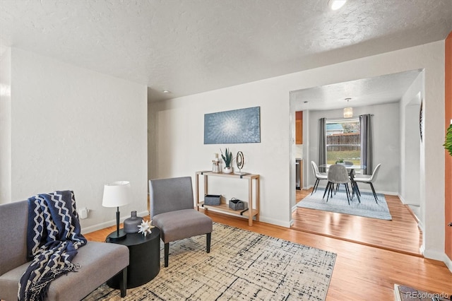 sitting room with baseboards, light wood-style flooring, and a textured ceiling