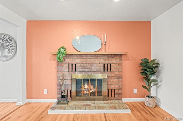 unfurnished living room featuring a brick fireplace, baseboards, and wood finished floors